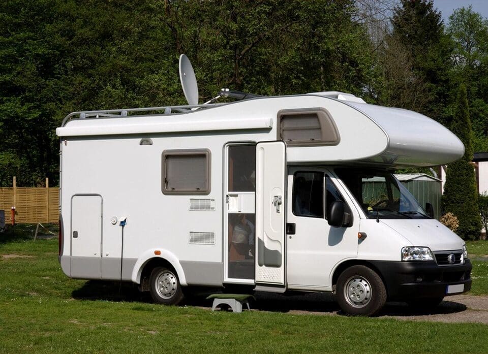 A white rv parked in the grass near some trees.