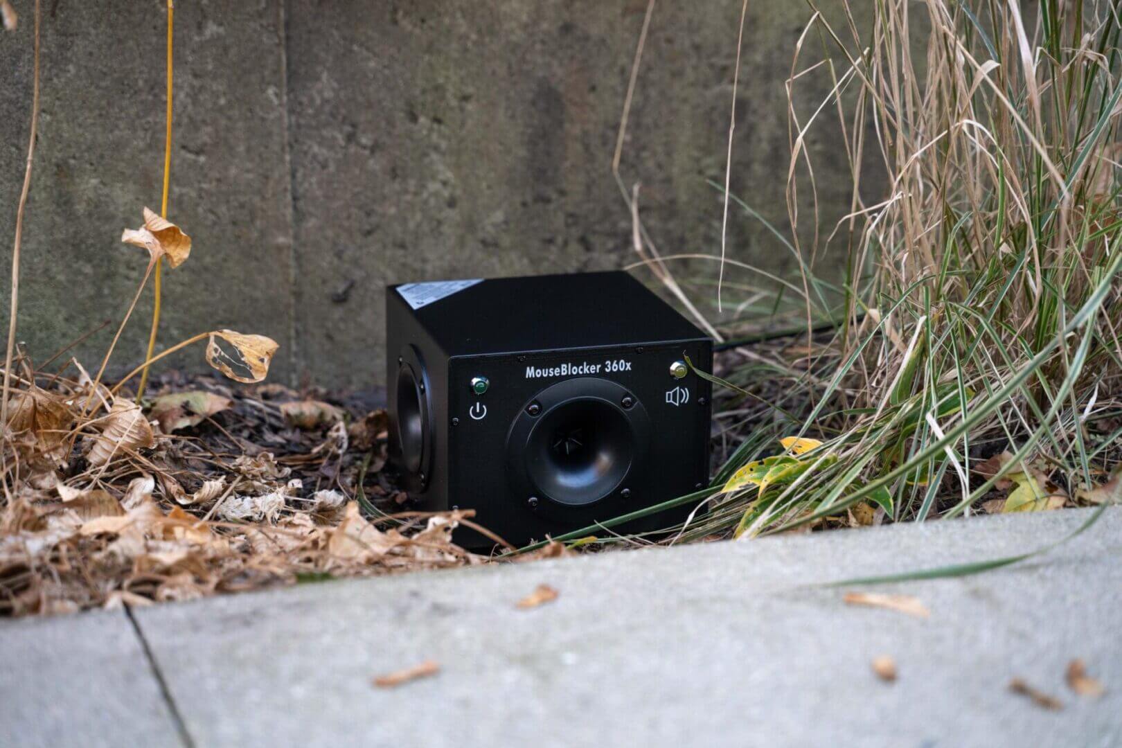 Black speaker device placed on outdoor ground.